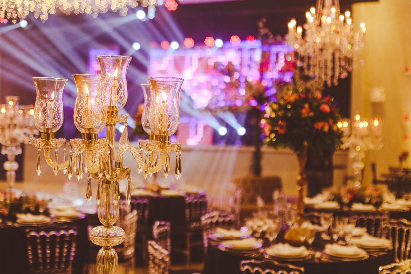 Ballroom with gold candelabra, chandeliers and warm stage lighting over dining tables